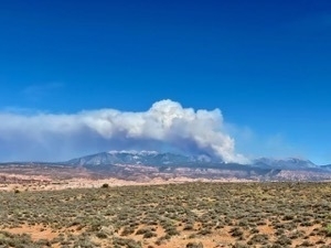 Photo of enormous wildfire burining in the distant moutnains as seen from Arches National Park near Moab Utah
